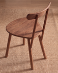 A Figura Dining Chair | Latte Oak by Wooden Stories, featuring a curved backrest and round seat, sits on a woven tan rug. This modern contract-grade dining chair has four legs and showcases a simple, minimalist design. The floor beneath is wood.