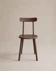 The Figura Dining Chair by Wooden Stories features a minimalist, modern design with a curved backrest, espresso oak finish, and contract grade durability, set against a neutral beige background.