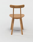 The Figura Dining Chair by Wooden Stories, shown from behind in light oak, features a curved backrest and minimalist silhouette—blending heritage woodworking with modern design against a plain white background.