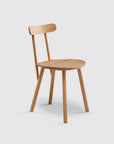 The Figura Dining Chair by Wooden Stories features a solid light oak build, four legs, a round seat, and a narrow curved backrest, highlighting heritage woodworking against a plain light gray background.