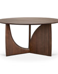 The Ethnicraft Geometric Dining Table in brown teak features a smooth round top and a distinctive base with curved and triangular forms.