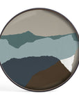 The Ethnicraft Graphite Wabi Sabi Glass Tray (Round/Extra Large) features an abstract design of layered, jagged organic shapes in blue, green, brown, and white that evoke mountain silhouettes and European refinement.