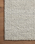 A close-up of the Loloi Hendrick Rug - Ivory shows its chunky, braided, hand-woven wool texture on a medium-toned wooden floor.