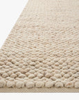Close-up of the Loloi Hendrick Rug - Natural, a beige hand-woven wool area rug with a chunky textured pattern and rounded edges, shown on a white background.