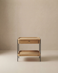 The Humla Side Table With Storage by Wooden Stories is a minimalist solid wood table with black metal legs, a single drawer, and an open lower shelf, shown against a neutral beige background.