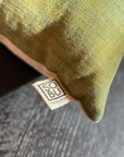 Close-up of the Alma de Oaxaca Cushion - Butterfly by SOBU, featuring a green handwoven design with a “SOBU OAKLAND” tag, set on a dark patterned surface.