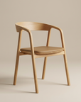 The Inlay Dining Chair by Wooden Stories features light oak, a curved backrest with armrests, a light brown leather cushioned seat, and four straight legs, all showcased against a neutral beige backdrop.