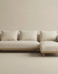 The Islet Modular Sofa | Fabric • M1 by Wooden Stories is a modern beige sectional with wooden legs, three back cushions, and a right-side chaise lounge, shown against a plain light background.