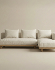 The Islet Modular Sofa | Fabric • M3 by Wooden Stories is a modern beige sectional with three large matching cushions, a right-side chaise lounge, a wooden base, and short wooden legs, displayed against a plain light background.