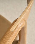 Close-up of the Wooden Stories Inlay Dining Chair in Light Oak and Leather. The image highlights its smooth solid oak armrest, seamless craftsmanship, and neutral leather seat from our Danish Collection, set against a softly blurred background.
