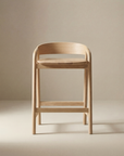 The Inlay Counter Stool | Wood Seat by Wooden Stories is a minimalist Danish stool with a curved backrest and smooth edges, crafted from solid oak. Set against a beige background, it’s ideal for stylish, modern kitchen island seating.