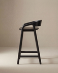 The Inlay Counter Stool | Wood Seat by Wooden Stories features a modern black solid oak design with a curved backrest and footrest, shown in profile against a beige background.