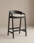 The Inlay Counter Stool | Fabric Seat by Wooden Stories features a solid oak frame, curved backrest, and light cushioned seat, set against a plain beige background.