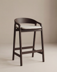 The Inlay Counter Stool | Fabric Seat by Wooden Stories features a curved solid oak frame and a light cushioned seat, shown against a plain beige background.