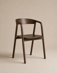 The Inlay Dining Chair | Wood from Wooden Stories, crafted in solid oak with a curved backrest and armrests, showcases clean lines and a smooth dark brown finish as it sits against a neutral beige background.