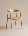 The Wooden Stories Inlay Dining Chair | Wood features a light oak frame with a curved backrest and armrests, showcased against a beige background. Its minimalist, modern design—marked by smooth, clean lines—captures the essence of the Danish Collection aesthetic. Combining elegance and durability, this solid oak dining chair by Wooden Stories offers timeless appeal for any dining space.
