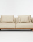 The Wooden Stories Islet Sofa | Leather is a modern beige sofa with durable leather, two seat cushions, two large backrest pillows, two smaller pillows, and a wooden base on a plain white background.