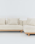 The Islet Modular Sofa | Fabric • M3 by Wooden Stories is a modern L-shaped beige sofa with a wooden base, four matching cushions, and a minimalist design, shown against a plain white background.