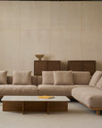 A modern living room features the Islet Modular Sofa | Fabric • M2 by Wooden Stories with plush cushions, a rectangular marble coffee table, a wooden side table, and two wooden cabinets against a neutral-toned wall.