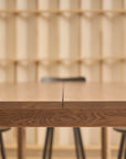 A close-up of the Wooden Stories Itamae Dining Table in Light Oak, paired with four black chairs and wooden shelves against a light wall, showcases a minimalist, modern space inspired by classic Danish design.