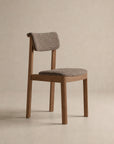 Introducing the Noki Dining Chair | Fabric by Wooden Stories—a modern solid wood chair featuring a textured, padded seat and backrest, both upholstered in light brown fabric and showcased against a plain beige background. Built to contract grade standards, this chair seamlessly blends style with durability, making it ideal for contemporary interiors.