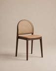 The Luk Dining Chair | Leather Seat by Wooden Stories, featuring a wooden arch silhouette, a curved cane weave rattan backrest, and a cushioned tan leather seat, is placed against a plain beige background.