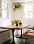 Bright, cozy breakfast nook with built-in bench seating, cushions, a wooden table with a fruit bowl, and the SOBU Cesco Dining Chair in White Ash. Wall shelves hold plants and decor as sunlight streams through two windows.
