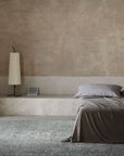 Minimalist bedroom with beige textured walls, a low bed with gray bedding, a modern pleated floor lamp, an Armadillo&Co Malawi Rug - Crane (Fair Trade), and a small square speaker. Light filters in through sheer curtains.