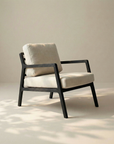 The Nysse Lounge Chair by Wooden Stories features a modern Scandinavian design with a black wooden frame and light beige cushions, set on a pale floor with soft natural light and gentle shadows creating a serene ambiance.