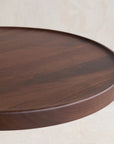 A close-up of the Bystander Side Table by Wooden Stories showcases its smooth, round dark wood tabletop with visible grain, set against a light neutral background.