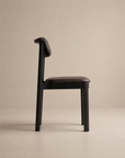 The Noki Dining Chair | Leather by Wooden Stories features a modern, minimalist design with a dark solid wood frame and brown leather seat and backrest—crafted to contract grade standards for lasting durability and style.