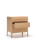 The Nell Tall Dresser from Wooden Stories features two drawers—one open and one closed—for stylish bedroom storage. Part of the Danish Collection, this light wood piece stands on four legs against a white background and is equipped with premium metal runners, seamlessly combining elegant design with practical functionality.