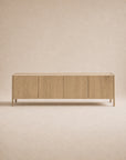 The Nell Sideboard | Blonde Oak by Wooden Stories is a minimalist wooden sideboard featuring four flat-panel doors, set against a beige background. Crafted from solid oak with a natural blonde finish, the cabinet showcases clean, straight lines and a modern, simple aesthetic inspired by Scandinavian design principles.