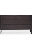 The Nell Wide Dresser by Wooden Stories features six horizontal drawers and is crafted with refined timber joinery in rich dark wood. Its simple lines and minimalistic design provide elegant bedroom storage, standing on four slender legs against a white background.