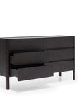 The Nell Wide Dresser by Wooden Stories is a dark wooden dresser from the Danish Collection, showcasing six spacious drawers—three of which are partially open to reveal exquisite timber joinery. Standing on four straight legs, this elegant piece is perfect for bedroom storage and is photographed against a plain white background.