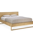 The Ethnicraft Nordic II Bed, crafted in solid European oak with a hardwax oil finish, features a rectangular headboard and light gray bedding with two matching pillows set against a plain white background.