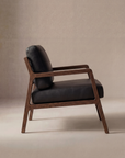 A side view of the Wooden Stories Nysse Lounge Chair | Leather showcases its Scandinavian design with a solid oak frame and black leather seat and backrest, set against a neutral beige background.
