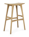 The Ethnicraft Osso Barstool - Oak features European styling with a curved seat, angled legs, and smooth rounded edges. Crafted in solid oak with a natural finish, its minimalist modern design adds elegance to any space.