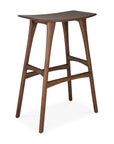 The Osso Barstool - Teak by Ethnicraft features FSC-certified teak, a curved seat, angled legs, and crossbar supports—all in a rich dark brown finish.
