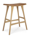 The Ethnicraft Osso Counter Stool blends European style and modern design, featuring a light solid oak frame, curved cognac leather seat, and four angled legs with horizontal supports for stability.