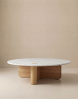 The Wooden Stories Pivot Coffee Table | Round - Wood & Stone features a white marble top and solid oak cylindrical base, shown against a plain beige background.