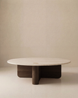 The Pivot Coffee Table | Round - Wood & Stone by Wooden Stories features a light stone top, dark solid oak base, and minimalist Danish-inspired design with clean lines, set against a plain beige background.