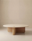 The Pivot Coffee Table | Round - Wood & Stone by Wooden Stories features a smooth light stone top and geometric solid oak base, offering a modern minimalist look inspired by the Danish Collection against a neutral beige background.