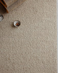 An Armadillo&Co Pebble Rug - Whippet in beige texture is spread on the floor, with a small metallic bowl holding three brown balls and a rolled-up piece of corrugated cardboard placed in one corner.
