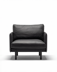 The Pensive Lounge Chair | Leather by Wooden Stories is a modern black leather armchair with Danish-inspired lines, cushioned seat and backrest, wooden legs, and a minimalist design, shown against a plain white background.