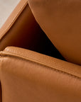 Close-up of a corner of the Pensive Sofa | Leather by Wooden Stories, highlighting its smooth, textured brown leather and detailed stitching. The background features a softly blurred, light-colored carpet.