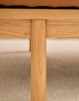 Close-up of a wooden leg attached to the frame of the Pensive Sofa | Leather by Wooden Stories, shown on a light textured carpet with a tan leather seat above.