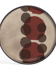 The Pinot Layered Dots Glass Tray - Round / Small by Ethnicraft features a beige glass surface with overlapping red and brown circles in various sizes, bordered by a dark rim.