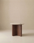 The Pivot Side Table by Wooden Stories features a round light stone top and a wood base with three curved legs, shown against a plain beige background.