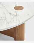 A close-up of the Pivot Coffee Table | Round - Wood & Stone by Wooden Stories, featuring a white marble top with gray veining, a circular wood inlay, and solid oak legs.